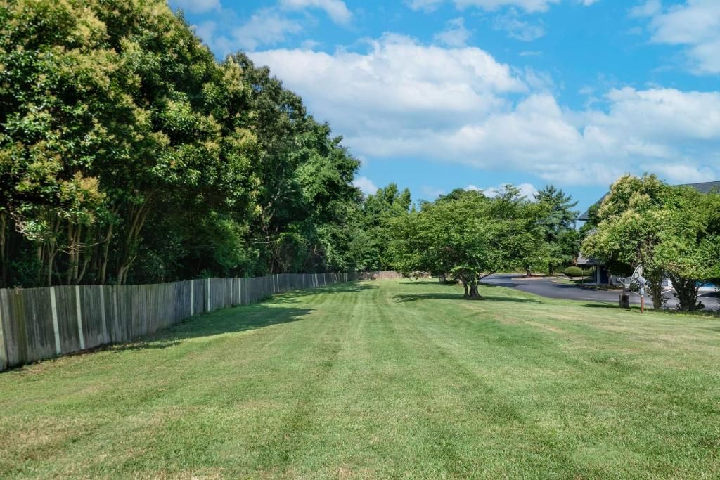A well-maintained grassy area with a wooden fence, trees, and a clear sky.