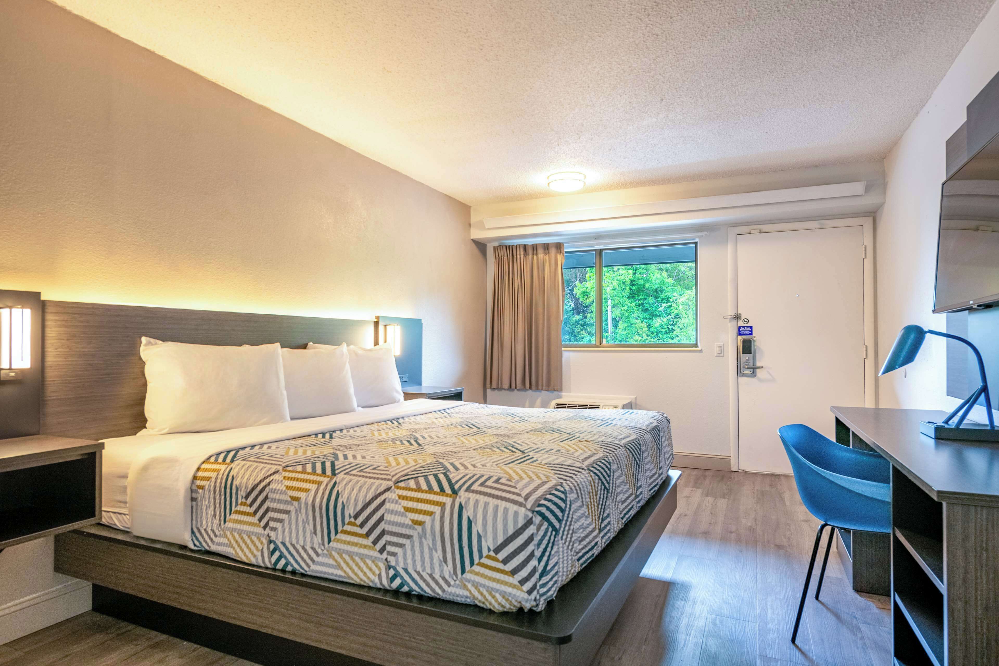 Una habitación de hotel con una cama, un escritorio, una silla y una ventana con cortinas.