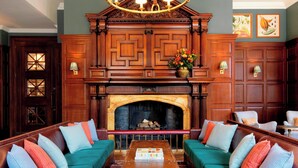 A traditional room with a fireplace, two green sofas with colorful cushions, a wooden coffee table, and a chandelier. - University Arms, Autograph Collection (Cambridge)