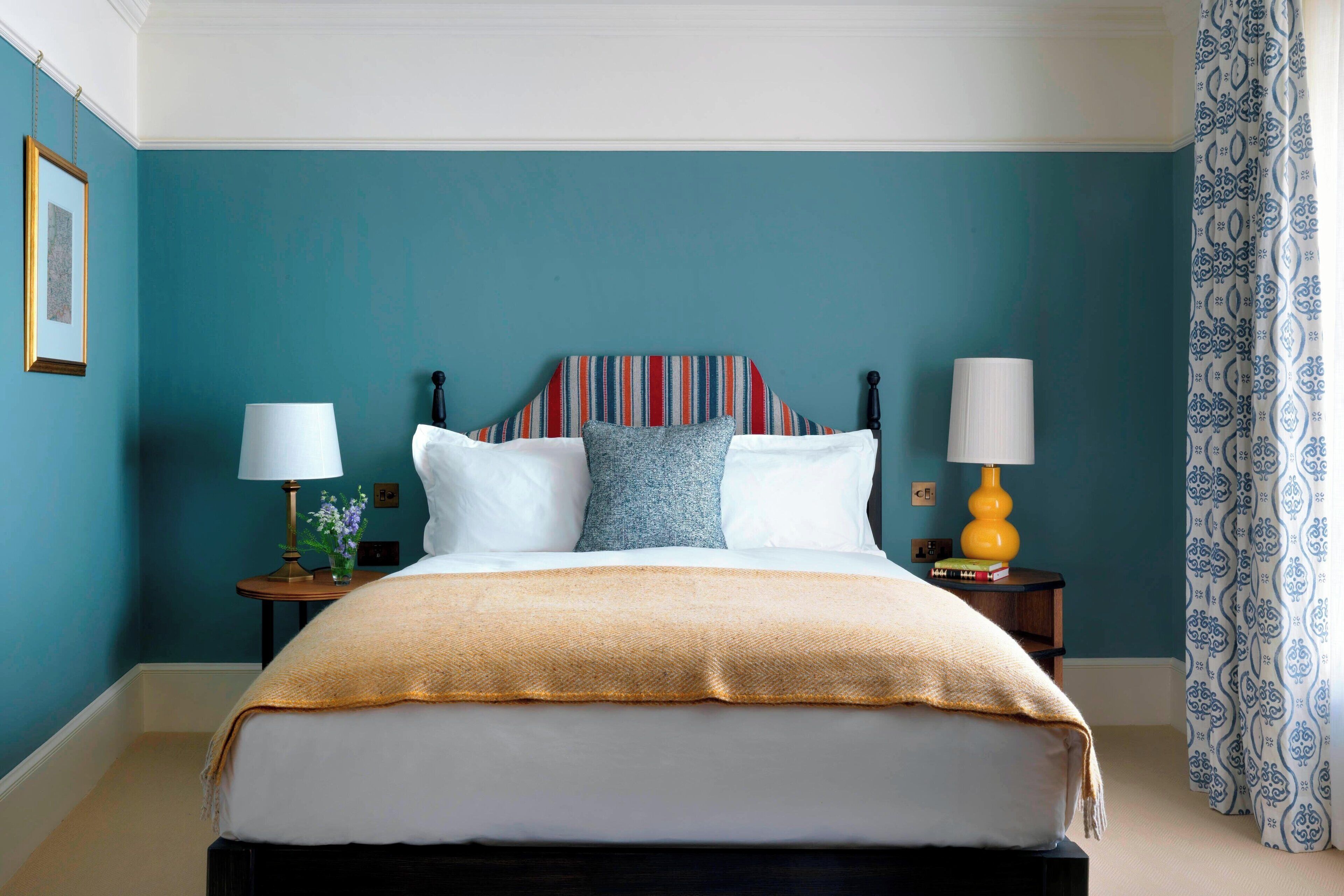A neatly made bed with a striped headboard, two bedside tables with lamps, and a patterned curtain.