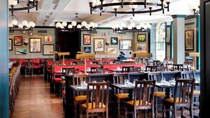 A restaurant with wooden tables and chairs, a long counter, and a chandelier. - University Arms, Autograph Collection (Cambridge)