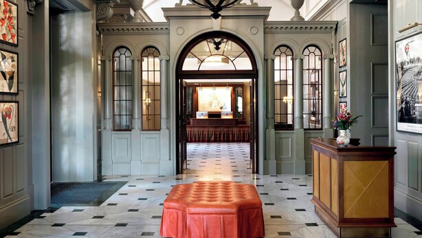 A grand hallway with a marble floor, a central red upholstered bench, and a reception desk. - University Arms, Autograph Collection (Cambridge)