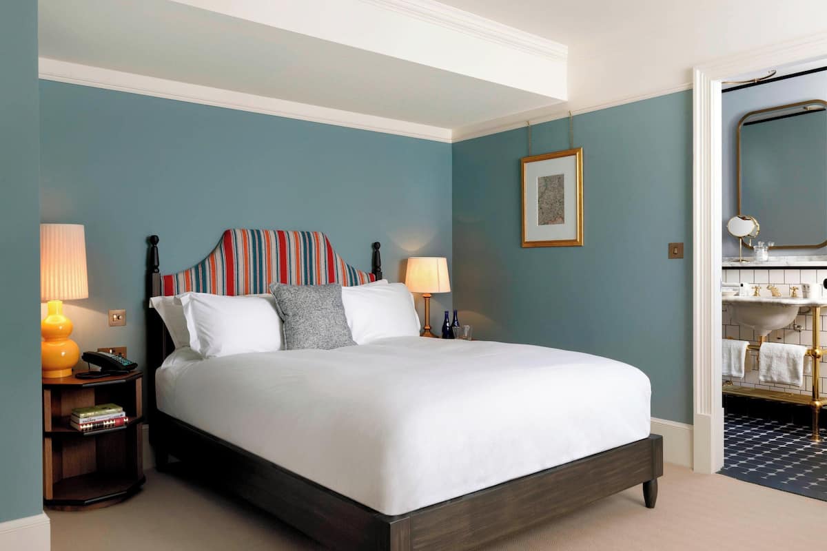 A neatly made bed in a room with teal walls, a wooden headboard, and a nightstand with a lamp and books.