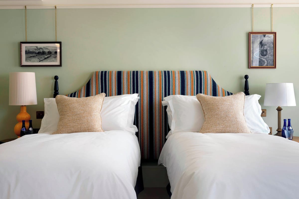 A hotel room with two beds, striped headboard, white bedding, lamps, and framed pictures on the walls.