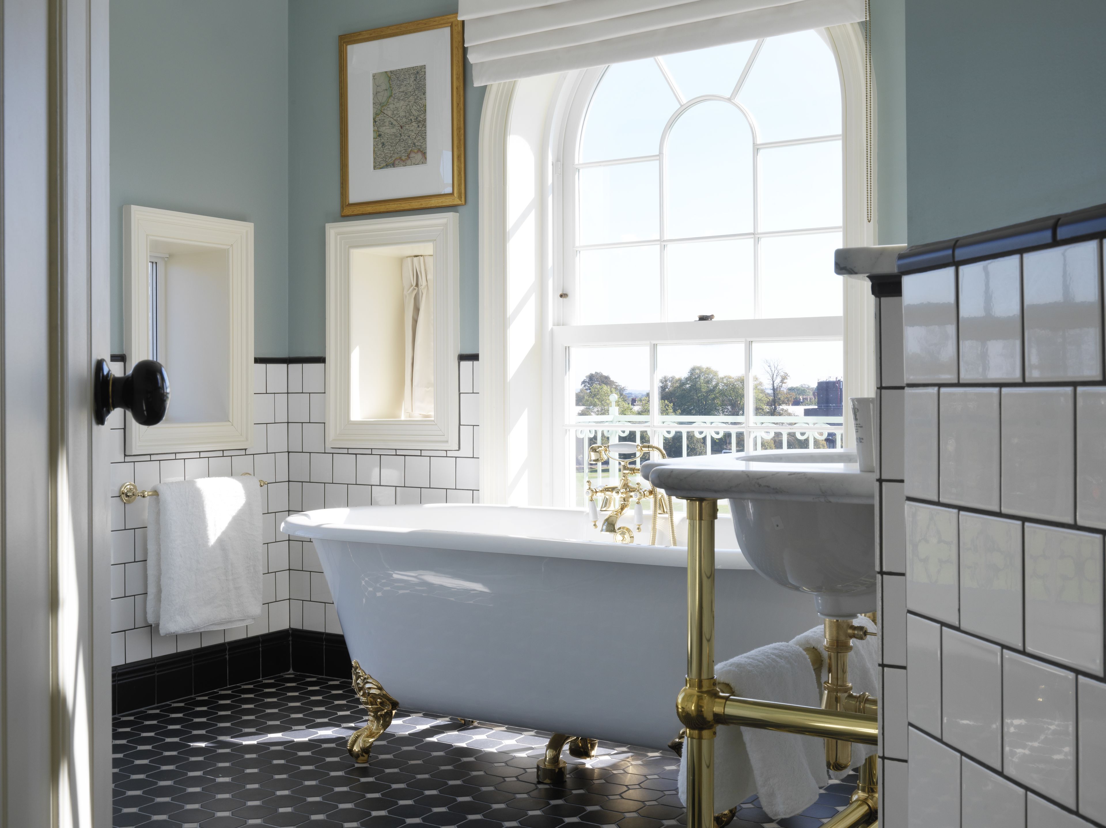 A bathroom with a freestanding bathtub, a gold faucet, and a window with a view of trees.
