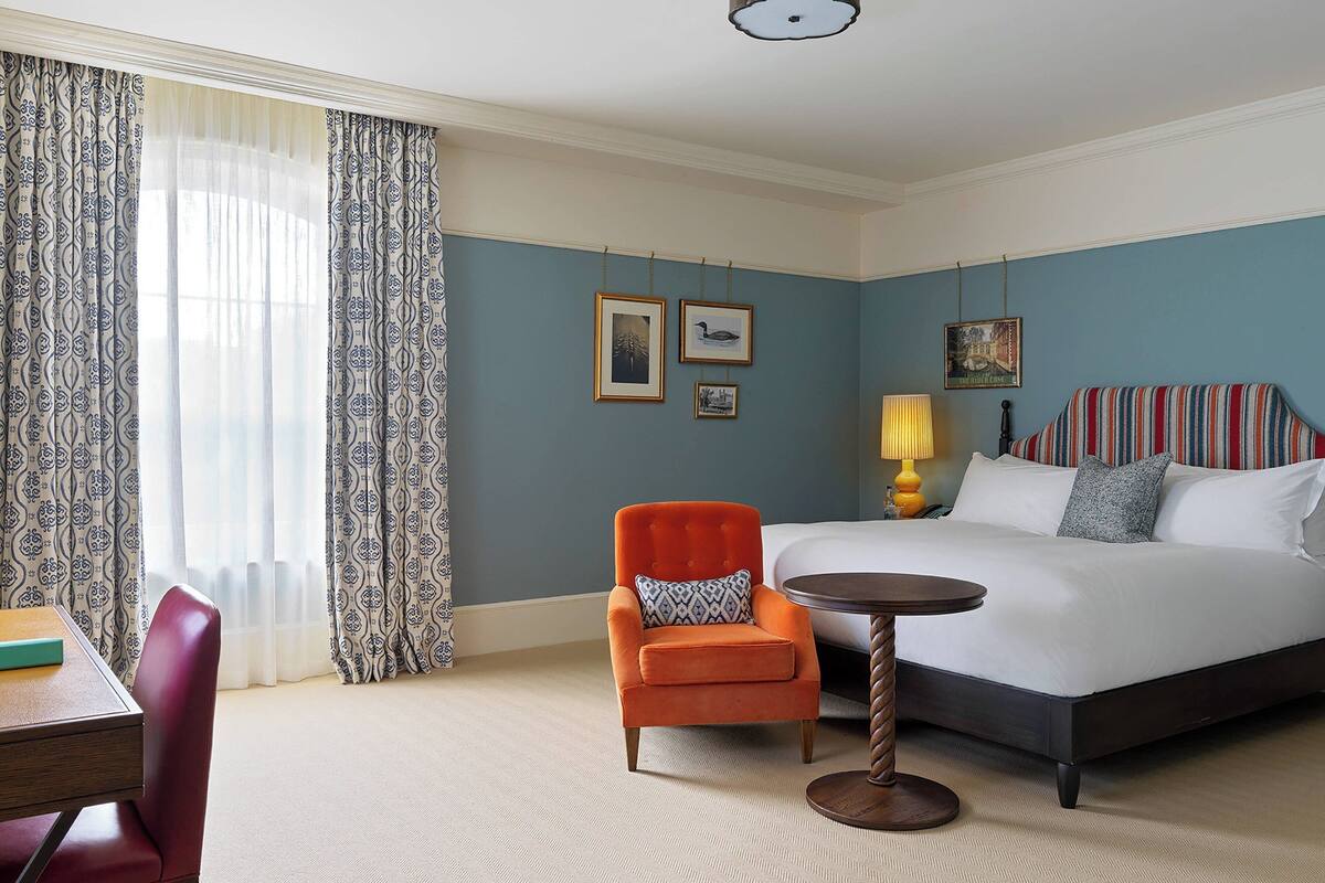 A hotel room with a bed, a chair, a table, and curtains.