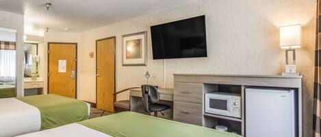 A hotel room with two beds, a desk with a chair, a television, a microwave, and a refrigerator.
