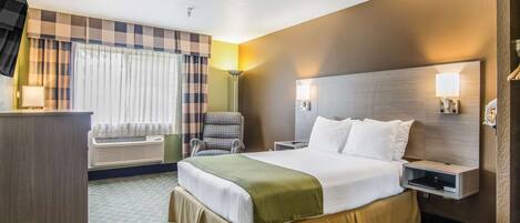 A hotel room with a large bed, a desk, a chair, a TV, and a window with curtains.