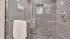 Un baño moderno con ducha de vidrio, una toalla blanca y un grifo de pared.