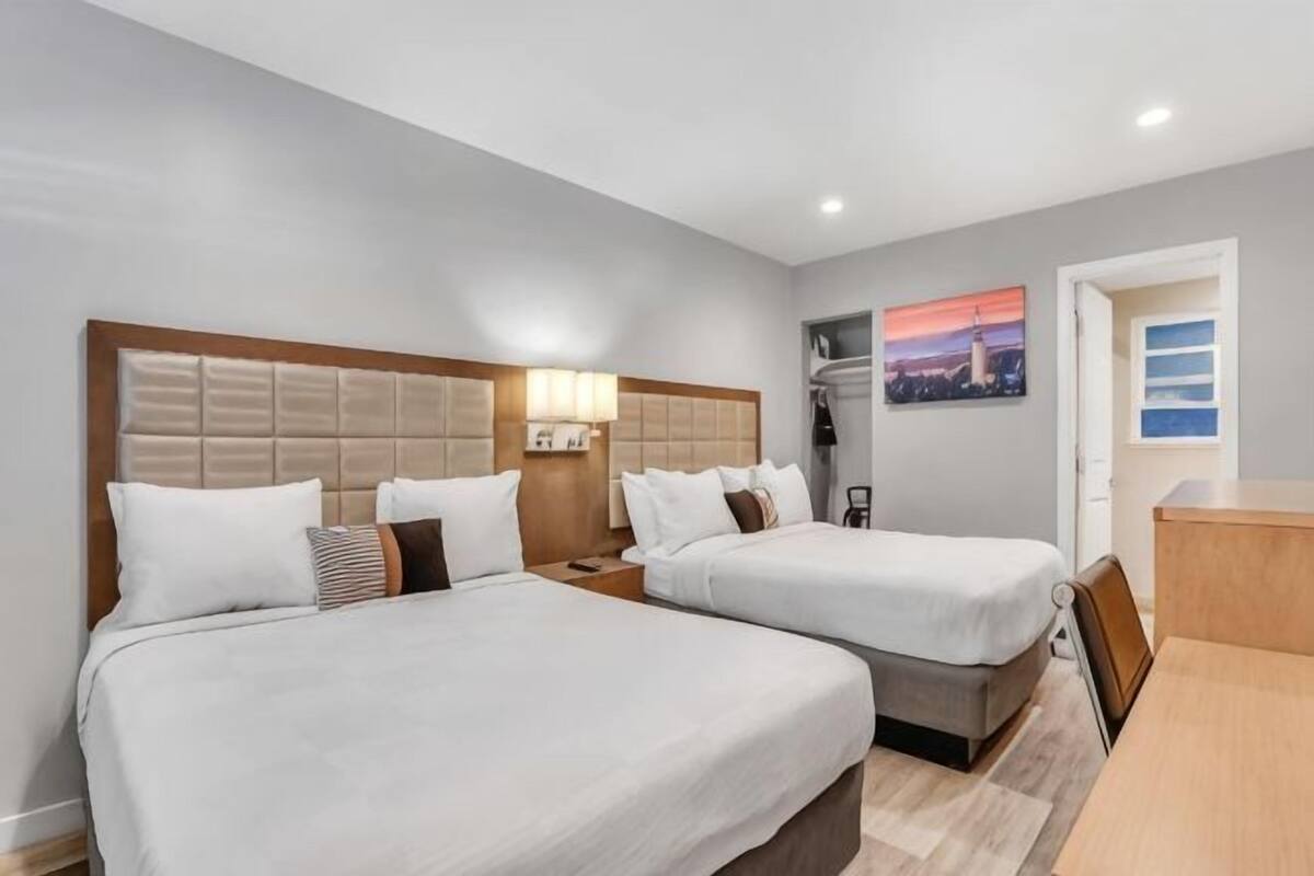 A hotel room with two beds, a desk, and a view of the cityscape.