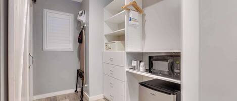 A compact kitchen with a microwave, a refrigerator, and a hanging coat rack.
