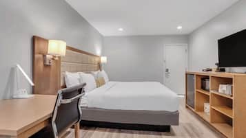 Habitación de hotel con cama, lámparas de noche, escritorio, silla, televisor y estante de madera con objetos.