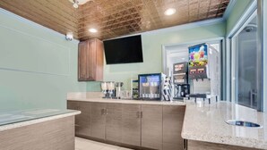 Una cocina con encimera de granito, armarios de madera, cafetera, refrigerador y televisor montado en la pared.
