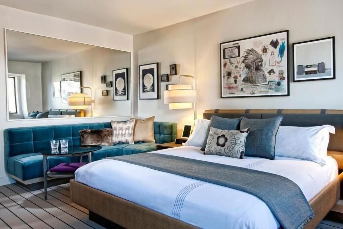 Una habitación de hotel moderna con una cama grande, un sofá azul, un escritorio y un espejo.