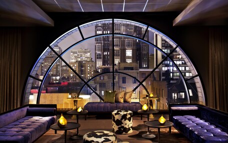 A modern lounge with a curved glass wall offering a city view, plush seating, and ambient lighting.