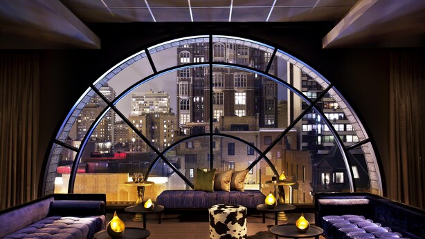 A modern lounge with a curved glass wall offering a city view, plush seating, and ambient lighting. - Thompson Chicago, by Hyatt (Chicago)