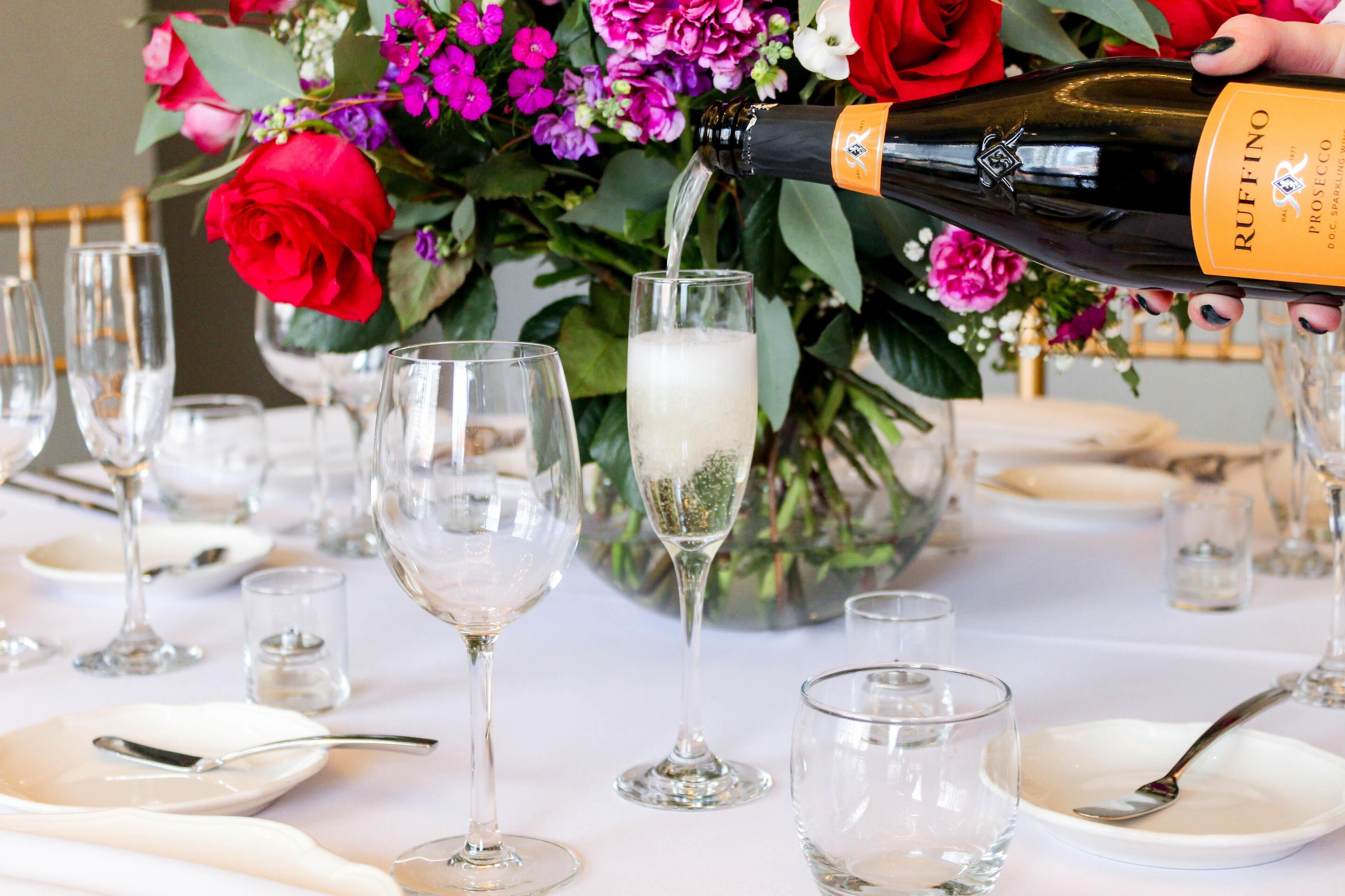 A table set for a formal event with wine glasses, plates, and cutlery, and a bottle of RUFFINO Prosecco being poured into a glass.
