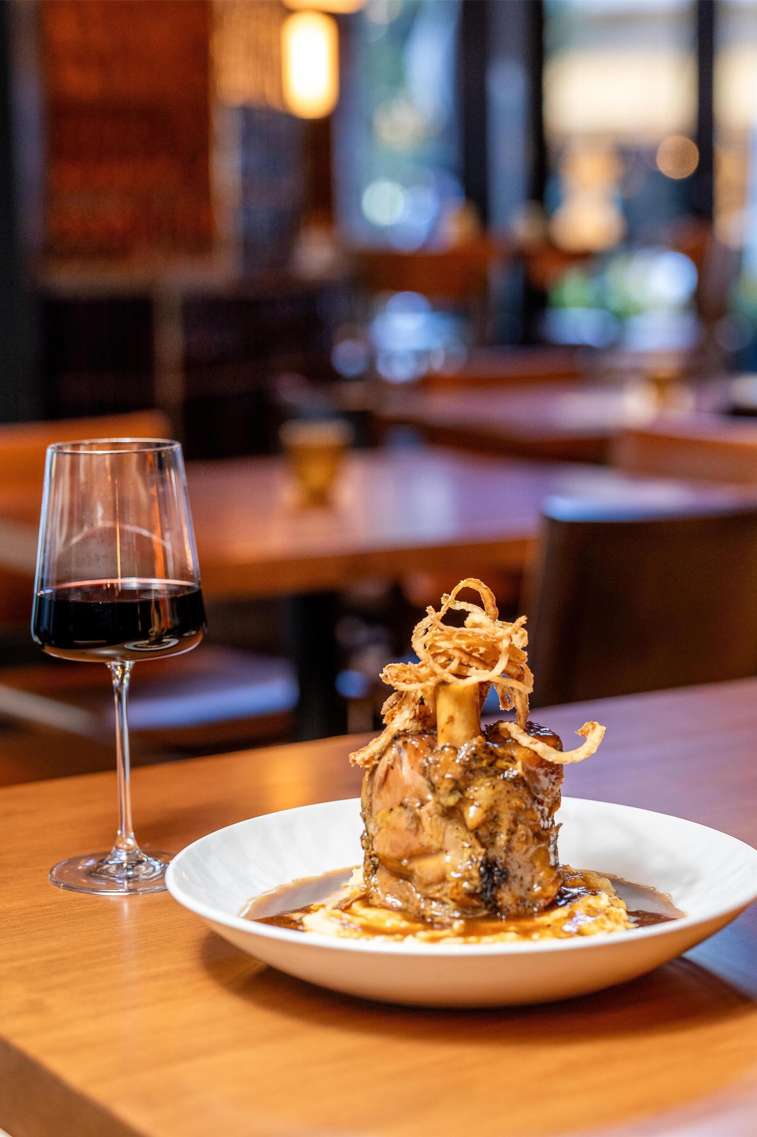 Una mesa de comedor con un plato de comida y una copa de vino tinto.