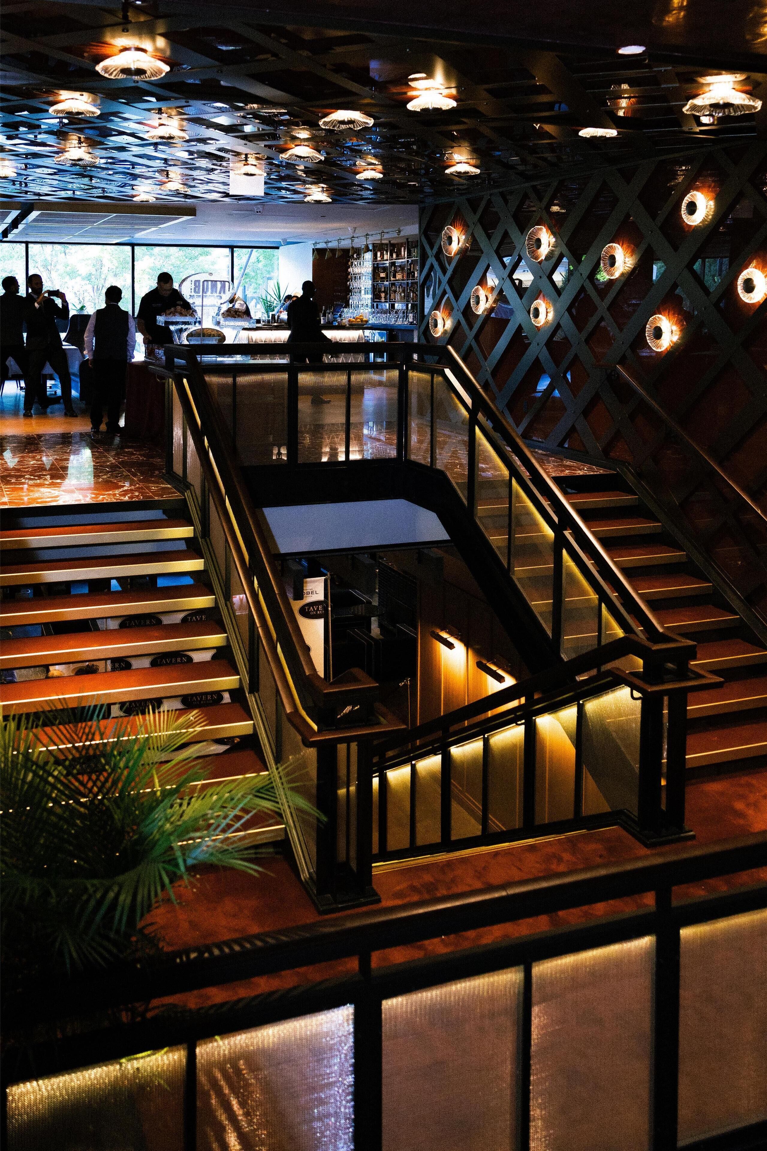A bar area with a staircase, wooden flooring, and a glass railing.