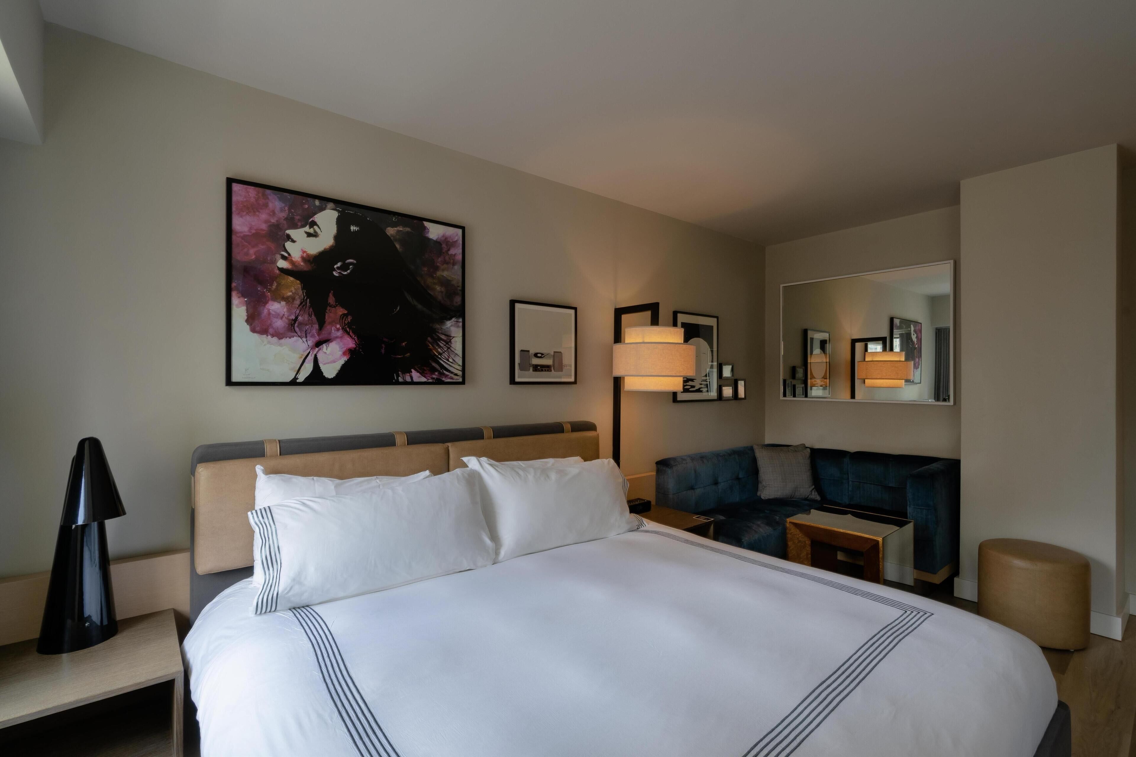 A hotel room with a large bed, a blue sofa, a desk, and a mirror.