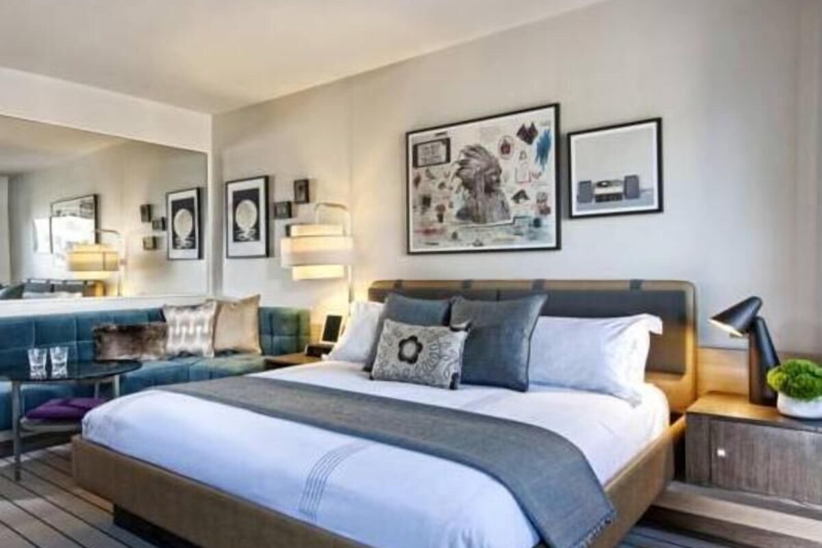Una habitación de hotel moderna con una cama grande, un sofá, un escritorio y una planta pequeña.