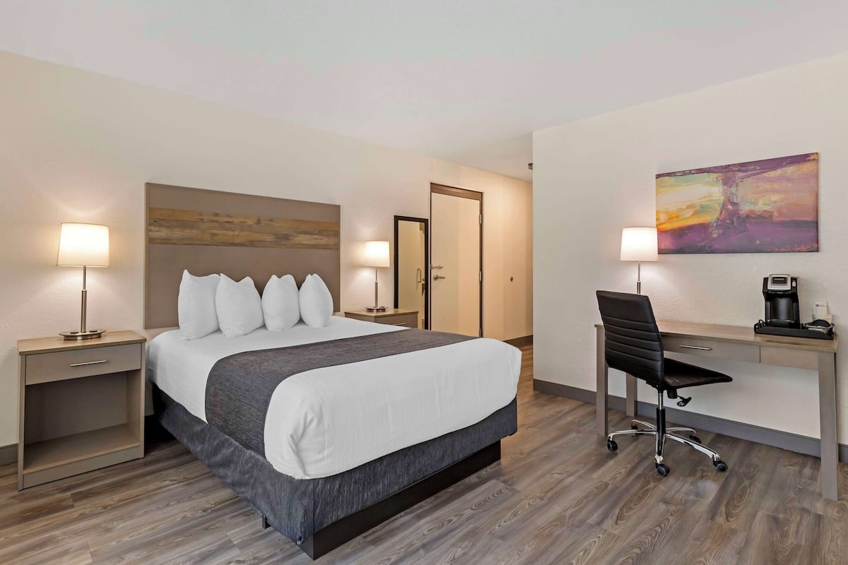A hotel room with a bed, bedside tables, a desk with a chair, a coffee maker, and a painting on the wall.