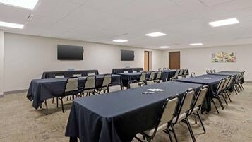 A conference room with multiple tables and chairs, a flat-screen TV mounted on the wall, and a carpeted floor.