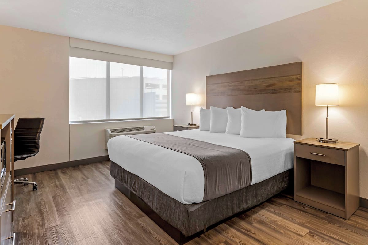 A hotel room with a large bed, bedside lamps, a desk, and a chair.