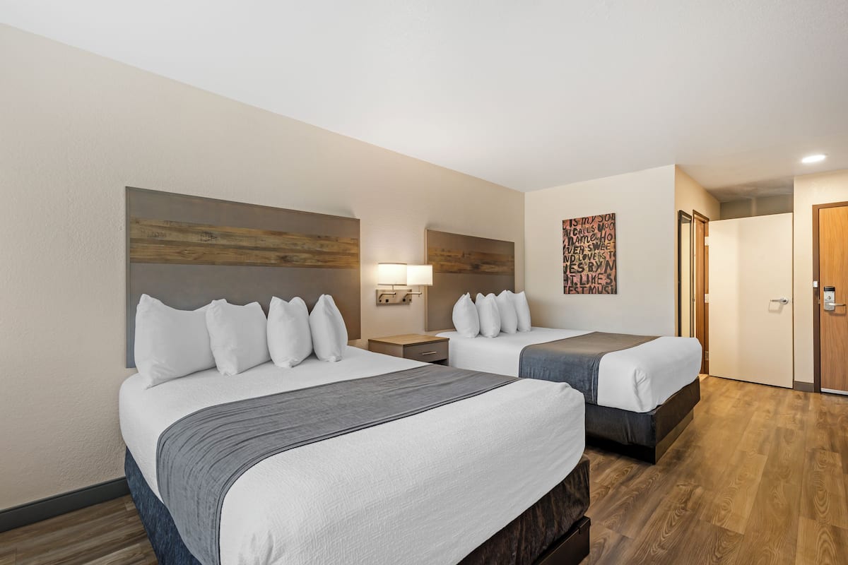 A hotel room with two beds, a wooden headboard, a wall-mounted light, and a door with a keypad lock.