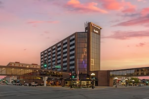 Un hotel con fachada de vidrio moderna, un letrero llamativo y un puente peatonal.