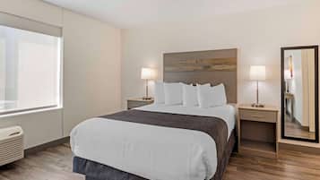 A hotel room with a large bed, two bedside tables with lamps, a large mirror, and a window.
