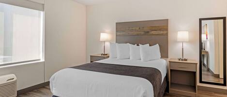 Una habitación de hotel con una cama grande, dos mesitas de noche con lámparas, un espejo amplio y una ventana.