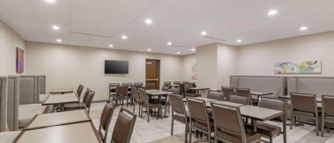 Un grand espace dédié à la salle à manger, avec plusieurs tables et chaises, un téléviseur à écran plat fixé au mur et des œuvres d’art accrochées aux murs.