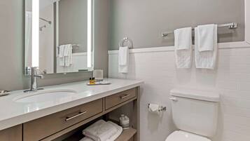 A modern bathroom with a white sink, mirror, and toilet. There are towels on the counter and hanging on the wall.