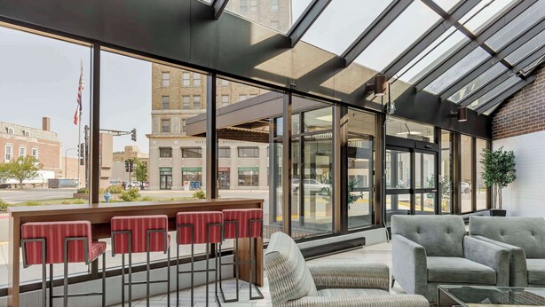 Un espace bar moderne avec de grandes baies vitrées, des tabourets de bar rouges et un coin salon doté de canapés gris.