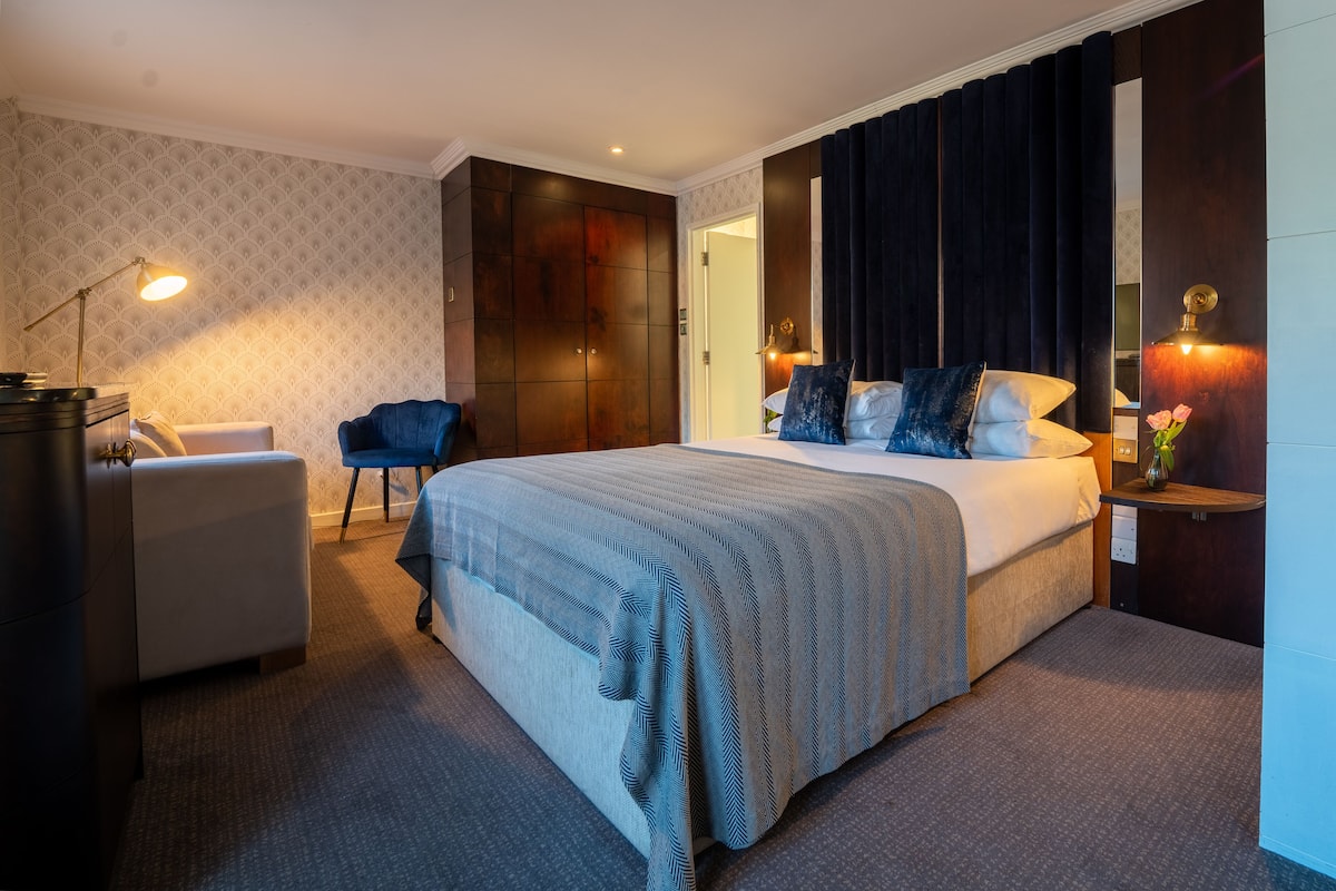Ein modernes Hotelzimmer mit einem großen Bett, einem Schreibtisch, einem Sessel und einem Kleiderschrank.