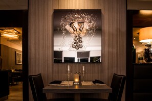 A dining area with a table set for two, a modern chandelier, and a decorative wall piece. - The Winchester Hotel & Spa (Winchester)