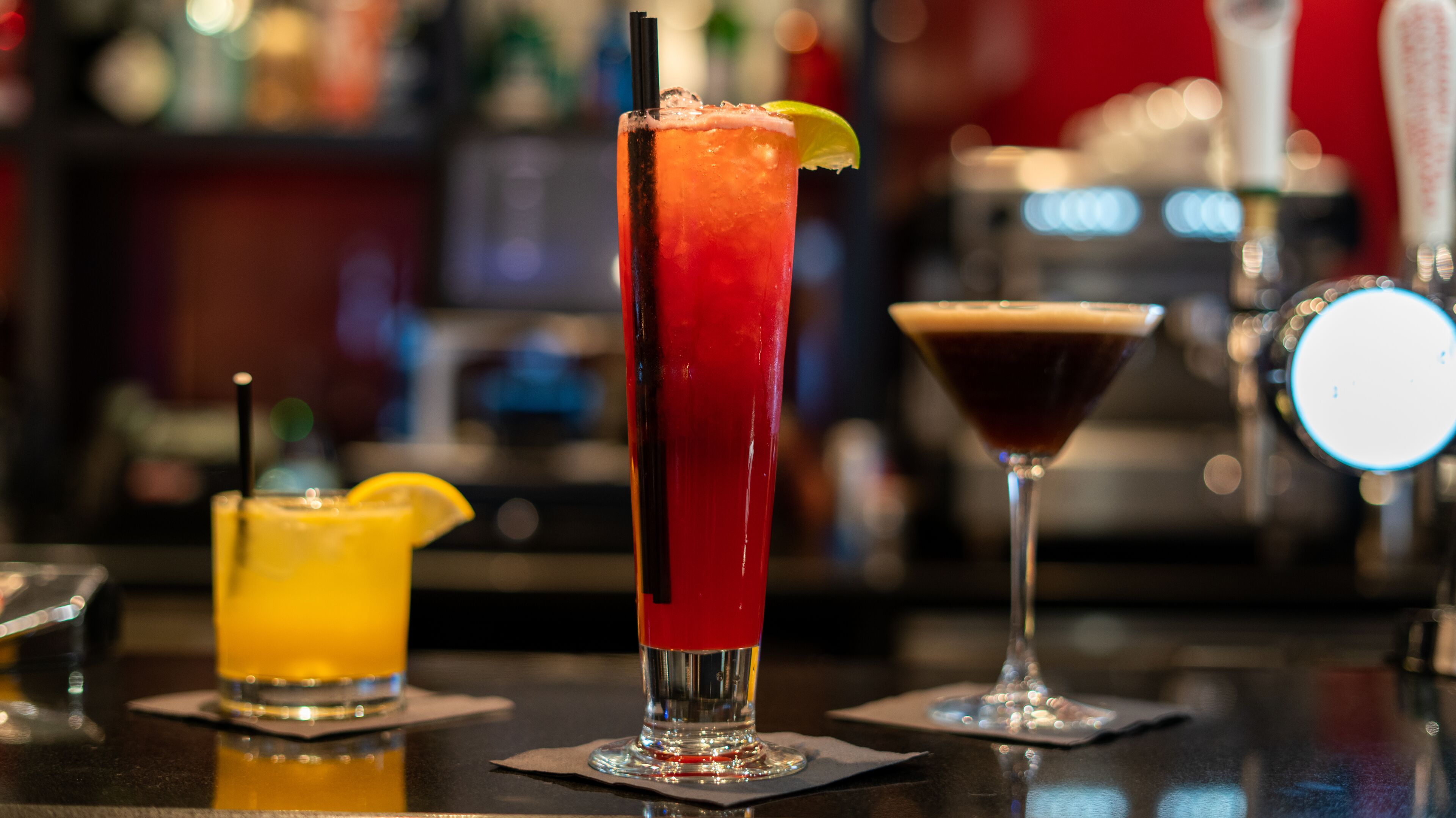 Three cocktails on a bar counter with a blurred background.