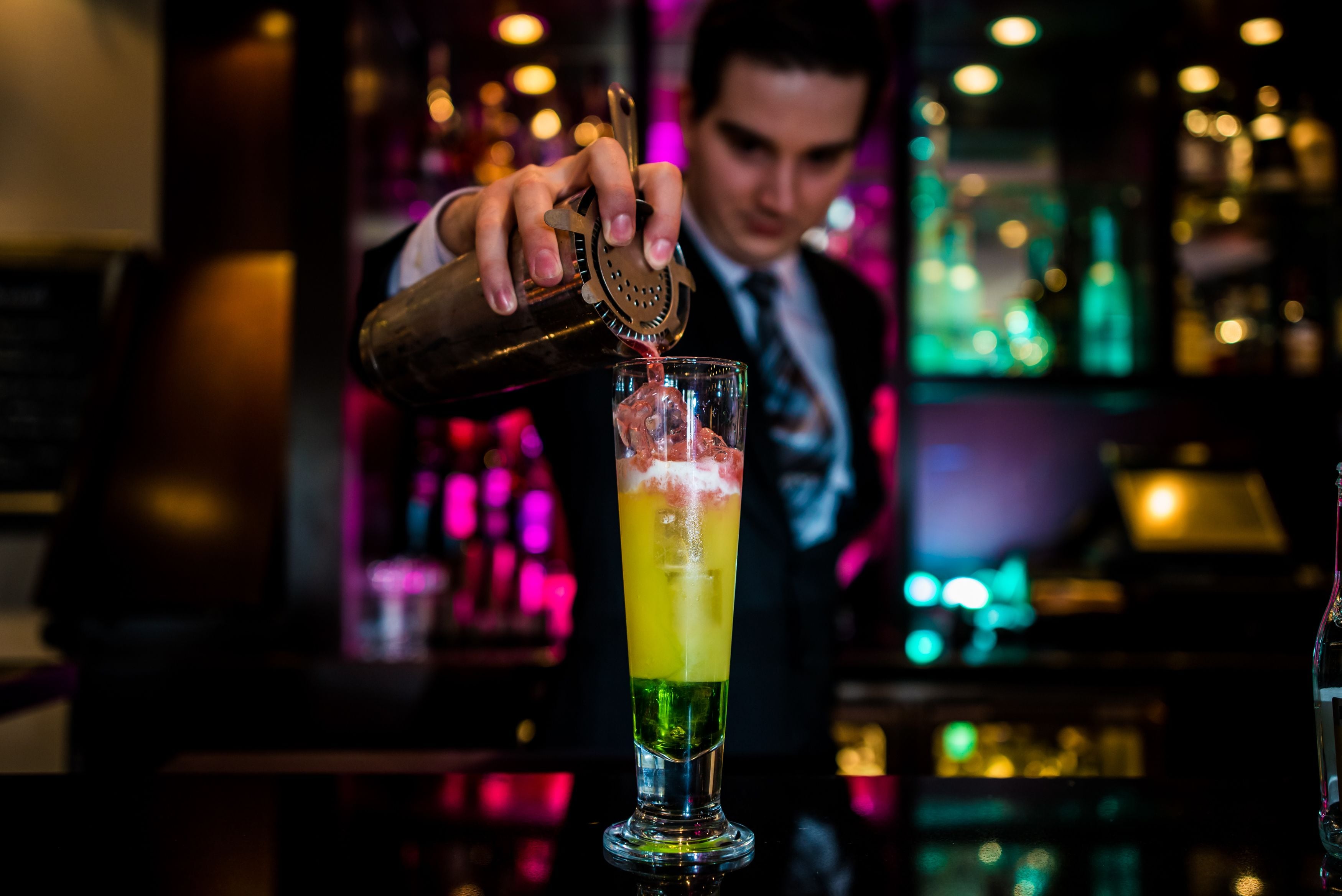 En bartender som häller upp en drink i ett högt glas.