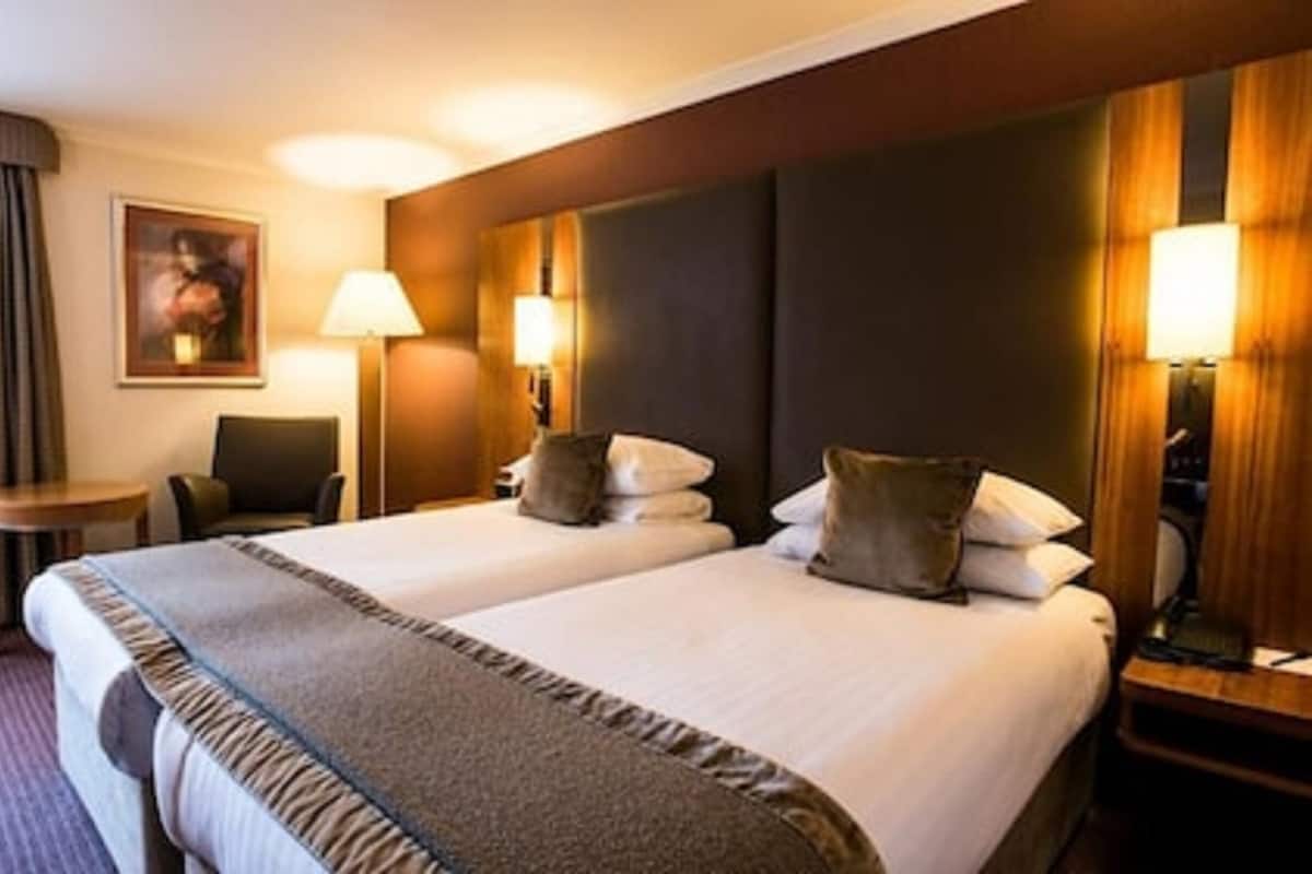 Ein Hotelzimmer mit zwei Betten, einem Schreibtisch, einem Stuhl und einem Bild an der Wand.