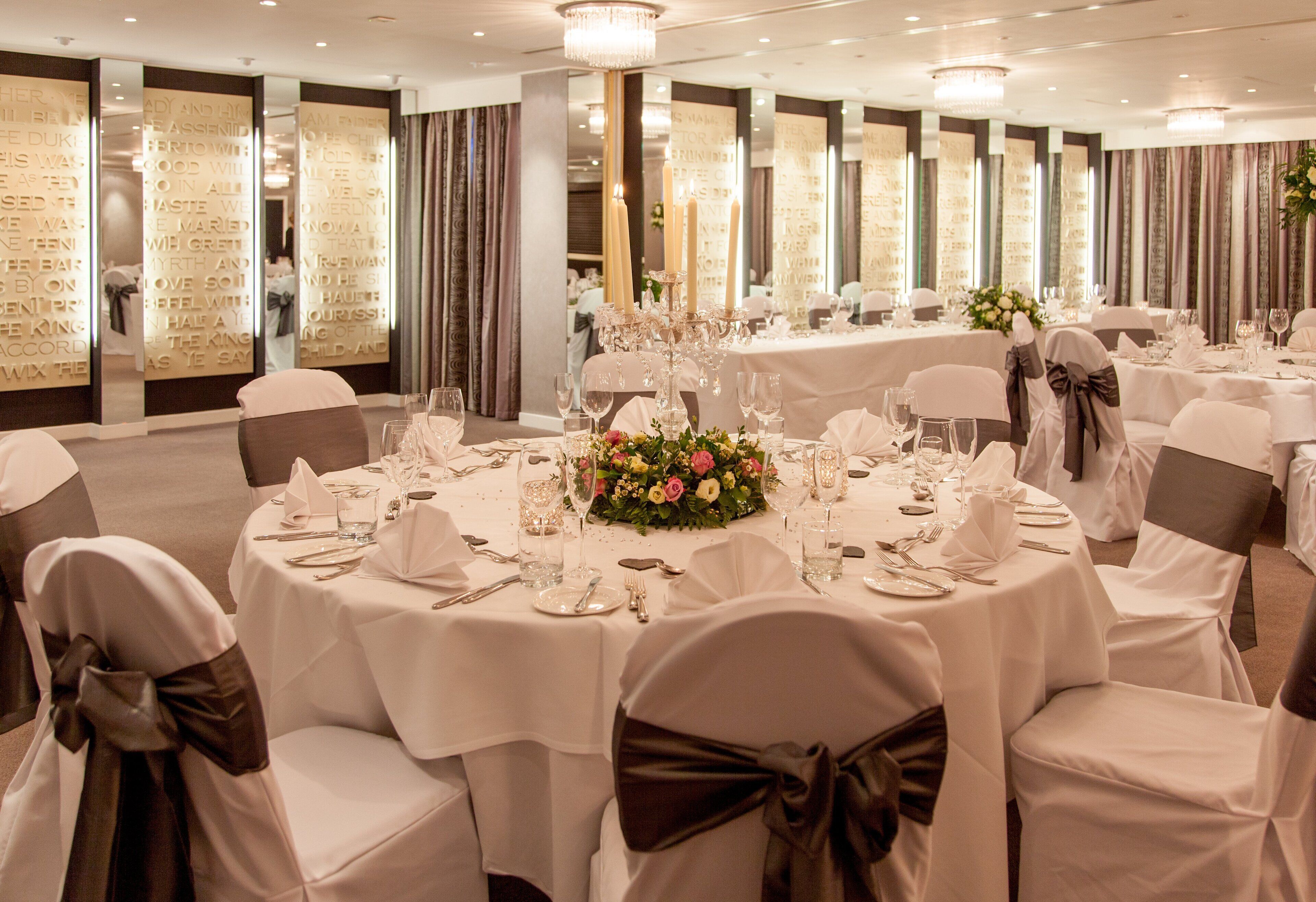 A banquet hall with round tables set for a formal event, each with white tablecloths, glassware, and floral centerpieces.
