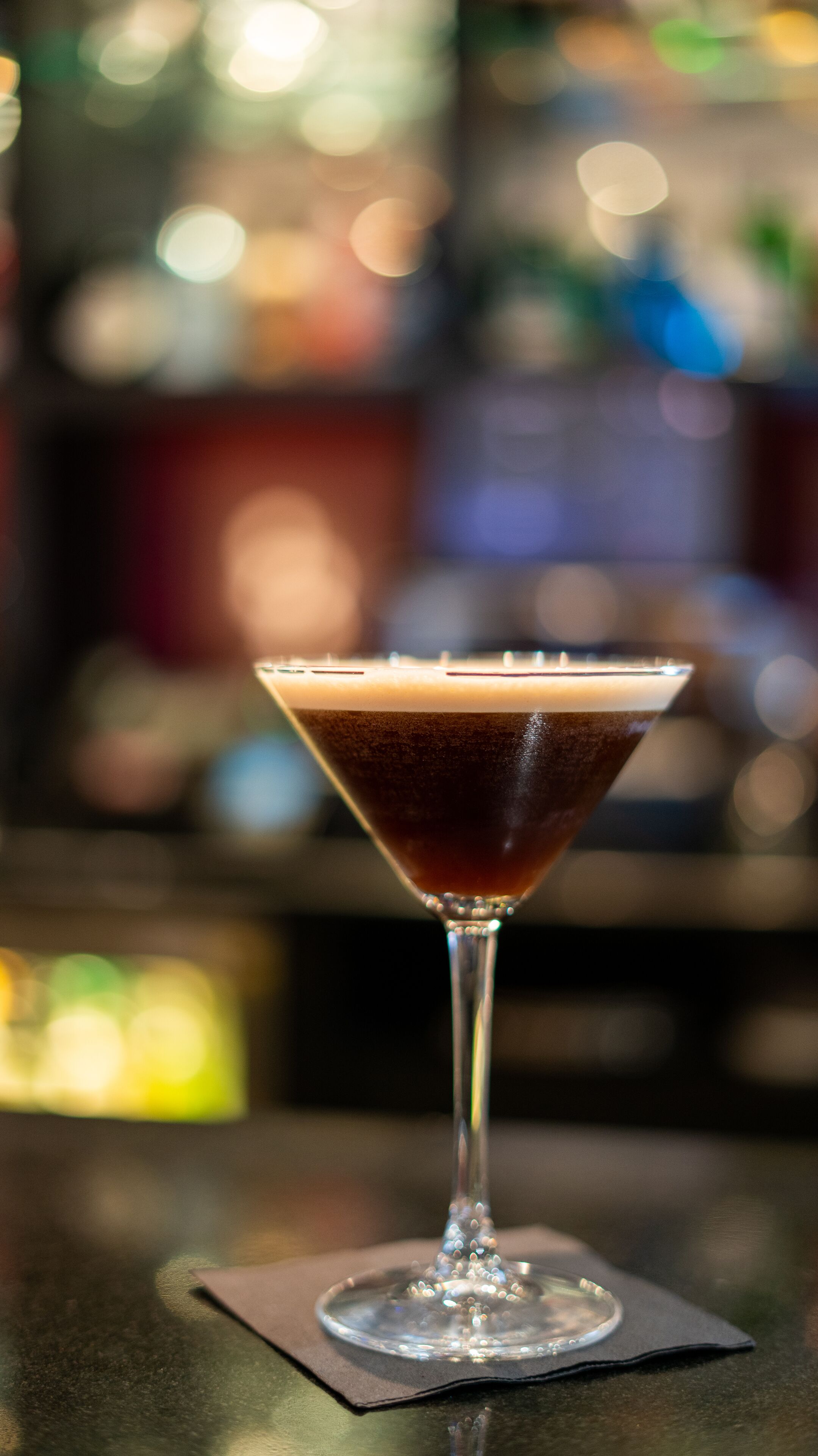 A martini glass with a dark liquid on a bar counter.