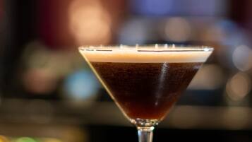 A martini glass with a dark liquid on a bar counter.