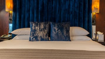 A hotel room with a large bed, dark blue curtains, two bedside lamps, and a wooden nightstand with a phone.