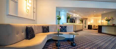 A modern hotel lobby with a curved sofa, round tables, and a patterned carpet.