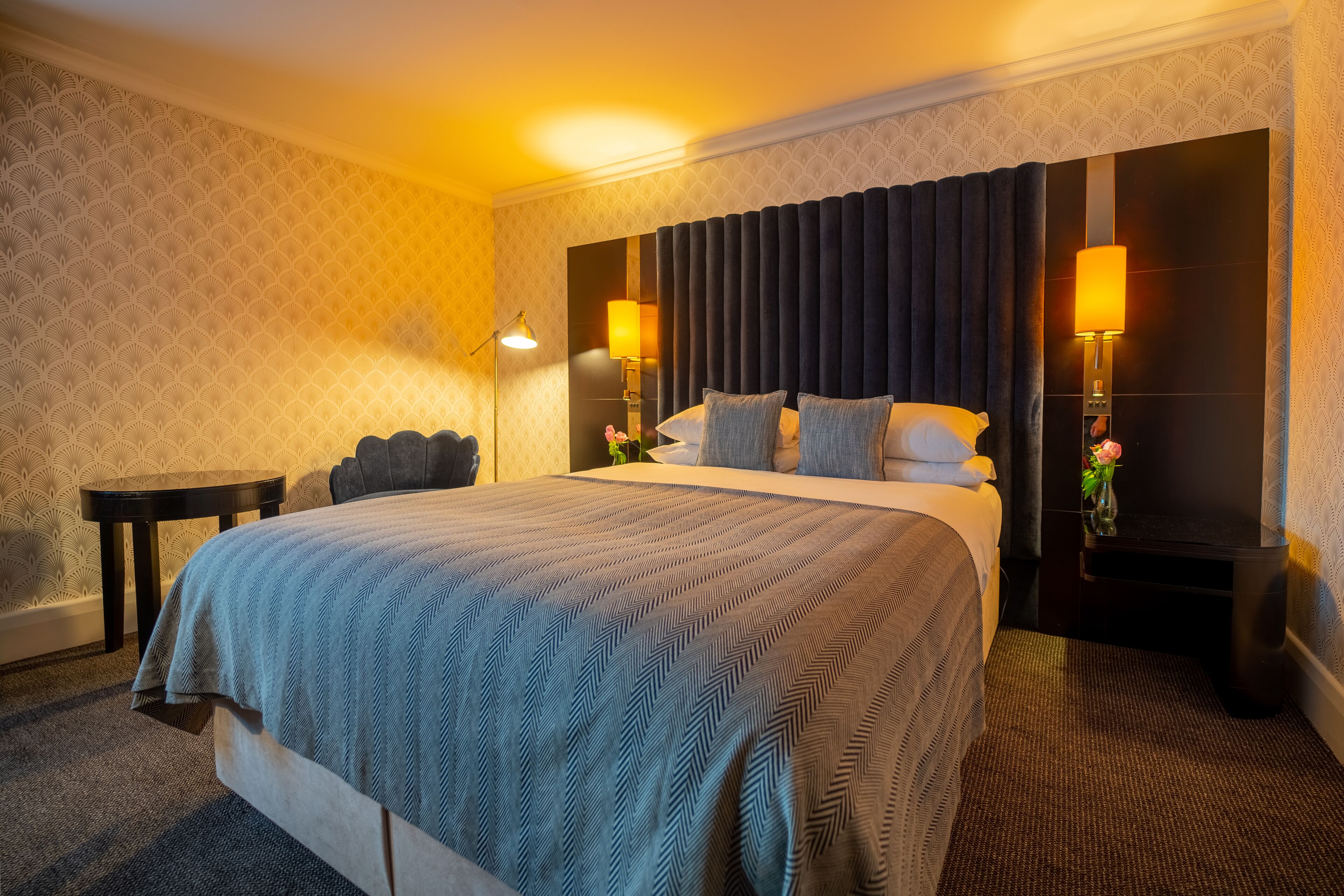 Hotellihuone, jossa on suuri sänky, kaksi yöpöytää, yölamppu ja peili.