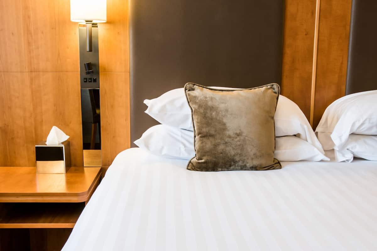 Ein Hotelzimmer mit Bett, Kissen, Nachttisch mit Lampe und Taschentuchbox.