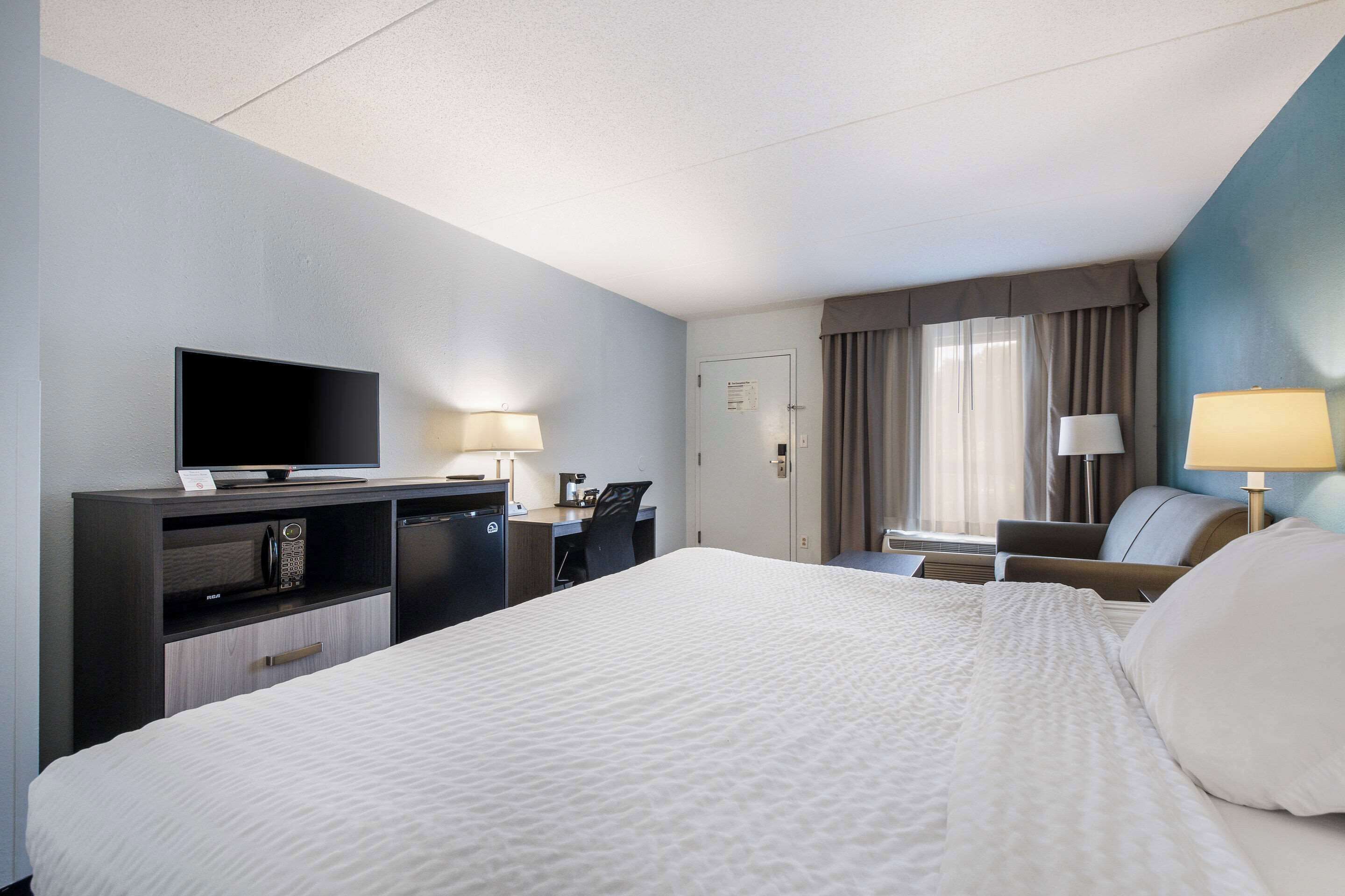 Une chambre d’hôtel comprenant un lit, un bureau avec un ordinateur, une télévision et deux lampes.