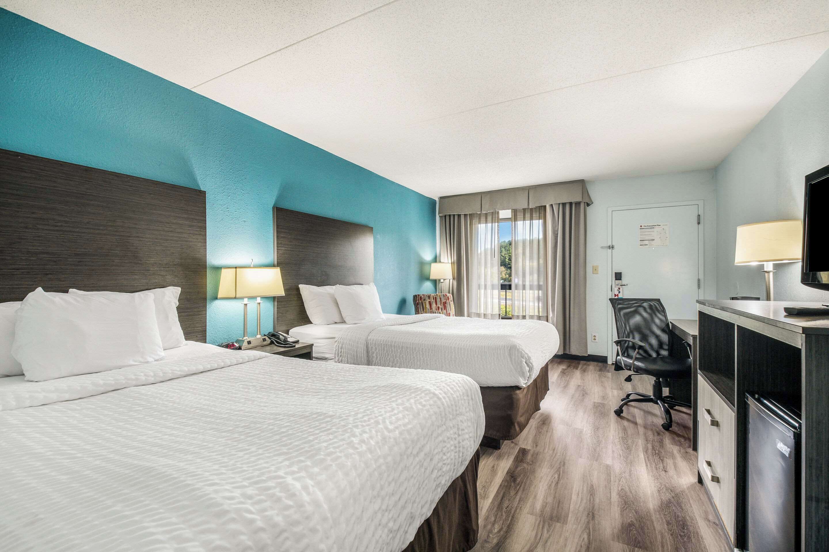 Habitación de hotel con dos camas, un escritorio, una silla, un televisor y una ventana con cortinas.