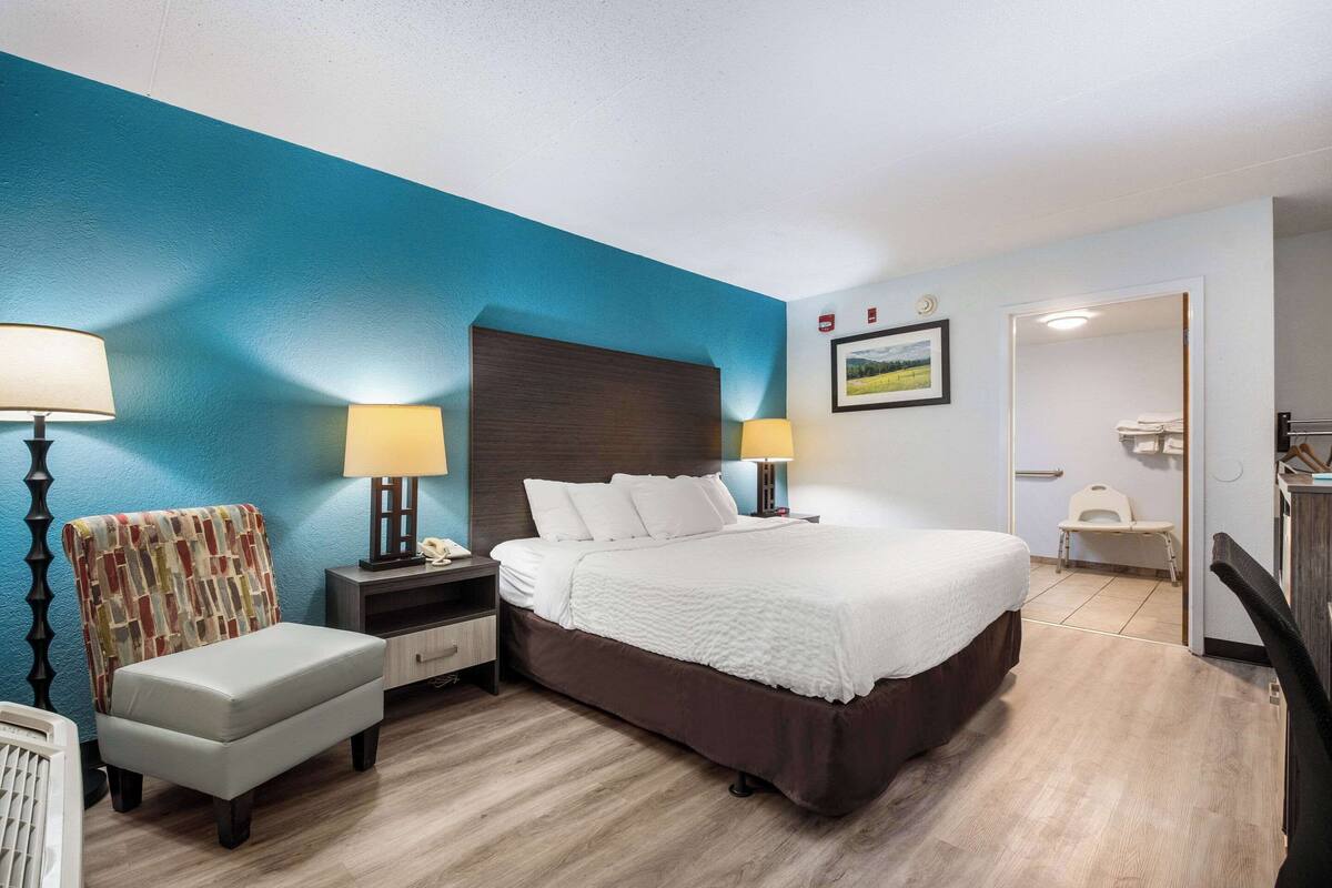 A hotel room with a large bed, two bedside tables with lamps, a chair, and a small desk.